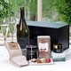 Prosecco Time Pamper Box. A curated gift arrangement featuring a bottle of prosecco, gourmet chocolates, a pair of cozy socks, skincare products, and a decorative box. The display is set on a table with greenery in the background. Prosecco Time Pamper Box. A curated gift arrangement featuring a bottle of prosecco, gourmet chocolates, a pair of cozy socks, skincare products, and a decorative box. The display is set on a table with greenery in the background.